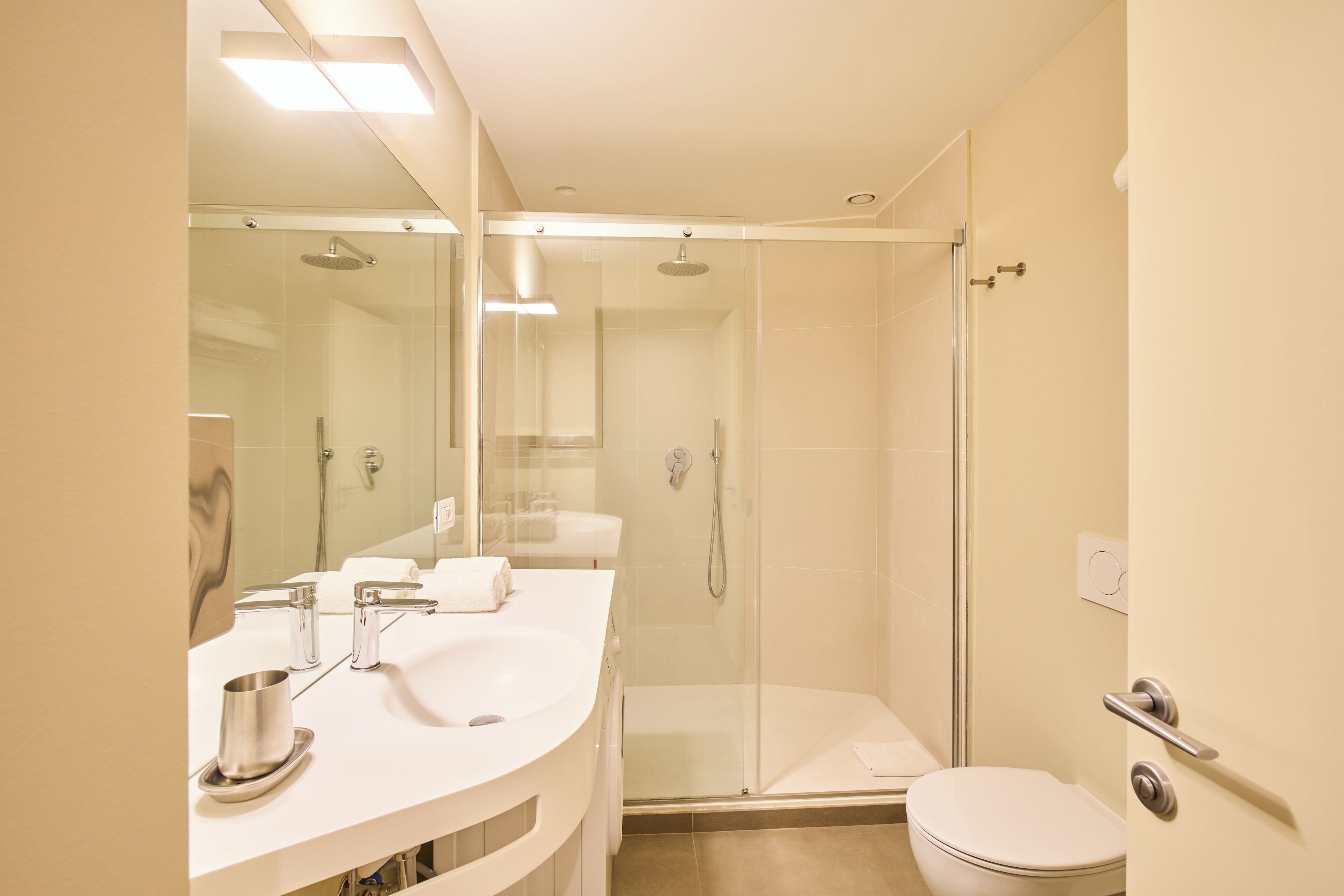 Un baño moderno con ducha envuelta en vidrio, un lavamanos blanco y un inodoro.