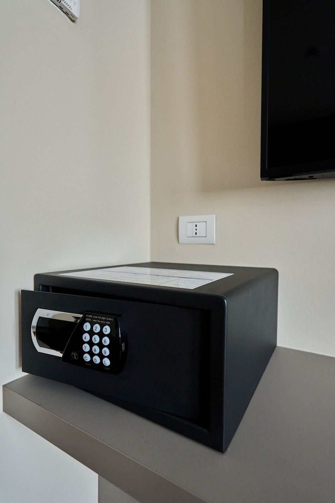 Un four à micro-ondes noir est posé sur un plan de travail, avec un clavier numérique, une prise de courant et un téléviseur fixé au mur au-dessus.