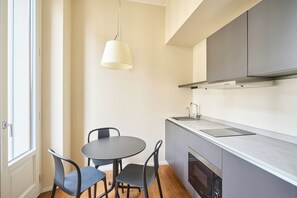 A compact kitchen with a dining table and chairs, a hanging light fixture, and a built-in oven. - Ariosto Living (Milan)