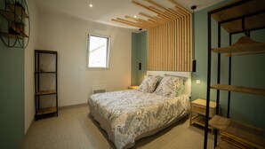 Ein Schlafzimmer mit Bett, Fenster, Ablagefläche und einer Wand aus Holzleisten.