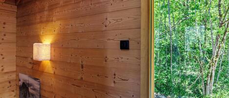 A wooden cabin interior with a wooden wall, a window, and a stone wall outside.