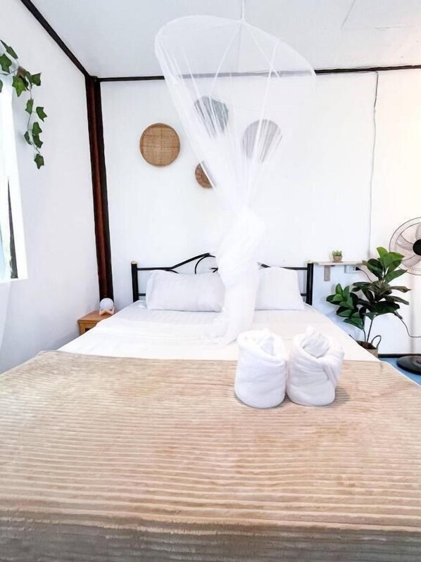 A neatly made bed with a white canopy, a bedside table with a small plant, and a wall-mounted fan.