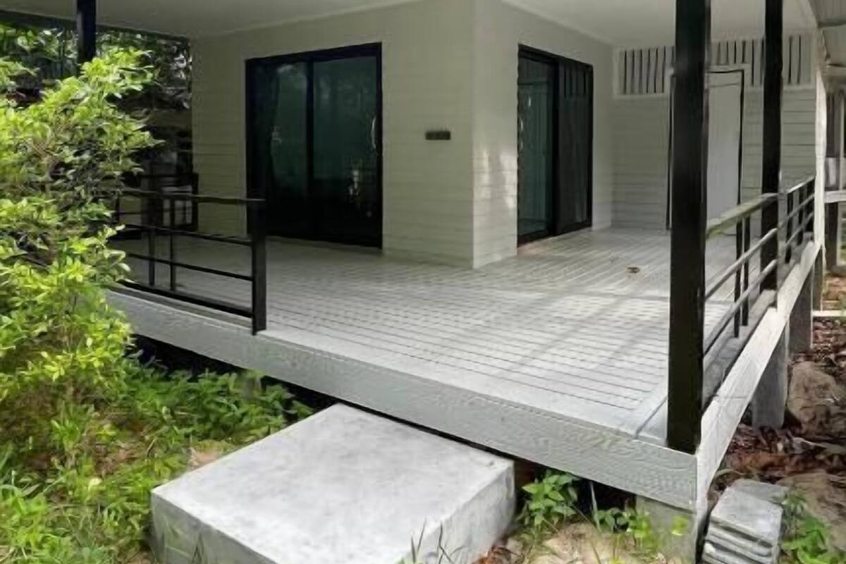 Ein modernes Haus mit überdachter Veranda, großen Glasfenstern und einem Steinweg, der zur Eingangstür führt.