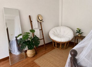 Une pièce avec un grand miroir, une chaise en rotin, une plante en pot et une petite table sur laquelle est posée une plante.