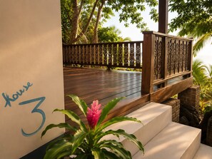 Una terraza de madera con barandilla, una escalera y una planta en maceta con flores rosas.
