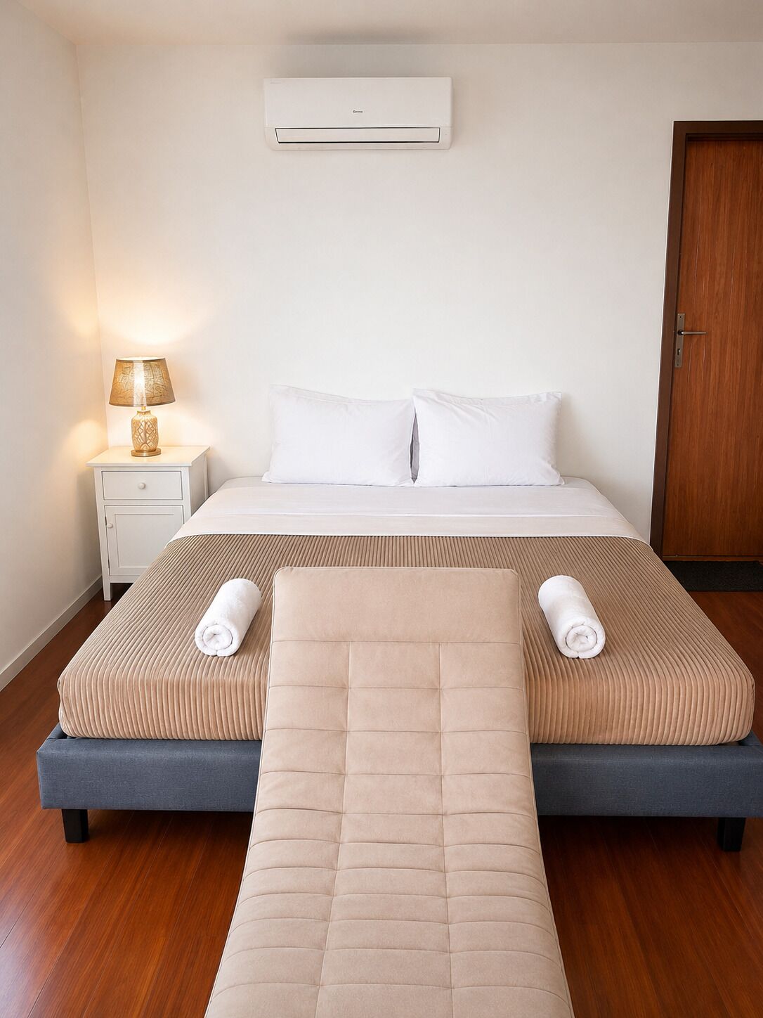 Una habitación de hotel con cama, mesita de noche, lámpara y aire acondicionado.