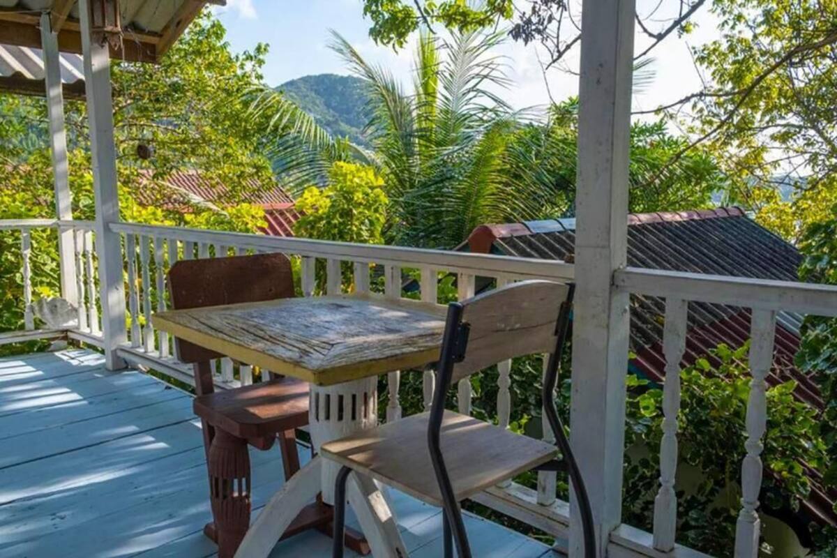 Eine Holzterrasse mit Tisch und Stuhl, umgeben von üppiger Vegetation und einem Berg im Hintergrund.