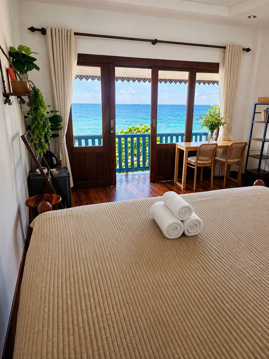 Een hotelkamer met een bed, een tafel met stoelen, uitzicht op zee en een balkon met gordijnen.