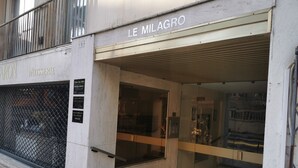 Een gebouw-ingang met een bord waarop 'LE MILAGRO' staat en een zichtbare etalage met een glazen gevel.