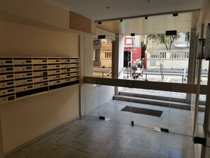 Ein Flur mit einer Reihe von Briefkästen, einer Glastür, die nach draußen führt, und einem Motorrad, das vor dem Gebäude steht.