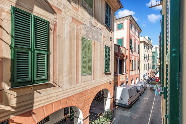A narrow street with historic buildings, green shutters, and parked vehicles.