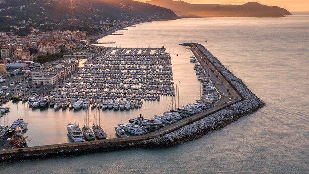 Ein Yachthafen mit zahlreichen Schiffen, einer Uferpromenade und einer Stadtlandschaft im Hintergrund.