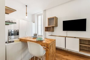 A modern kitchen with a wooden island, white chairs, a built-in oven, and a flat-screen TV mounted on the wall.