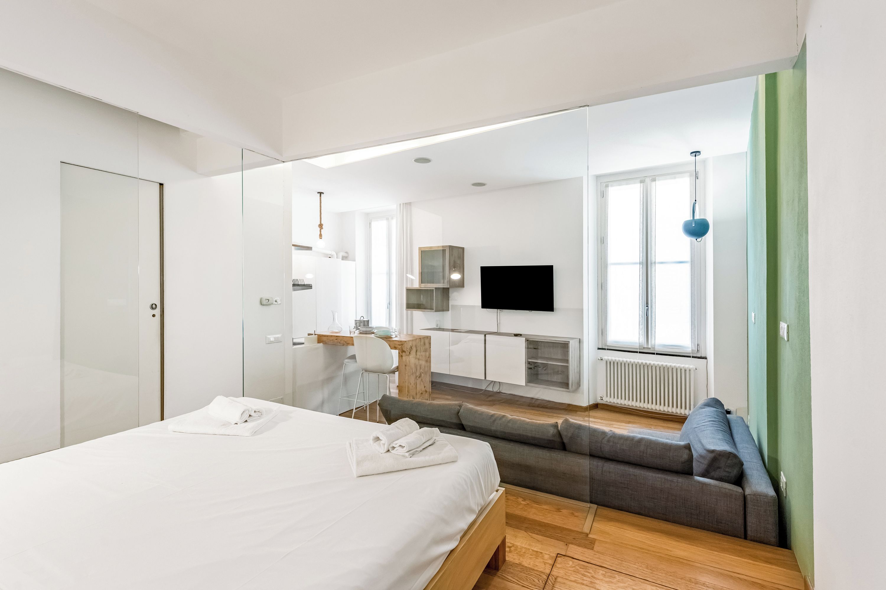 A modern hotel room with a bed, a sofa, a desk, a television, and a large window.