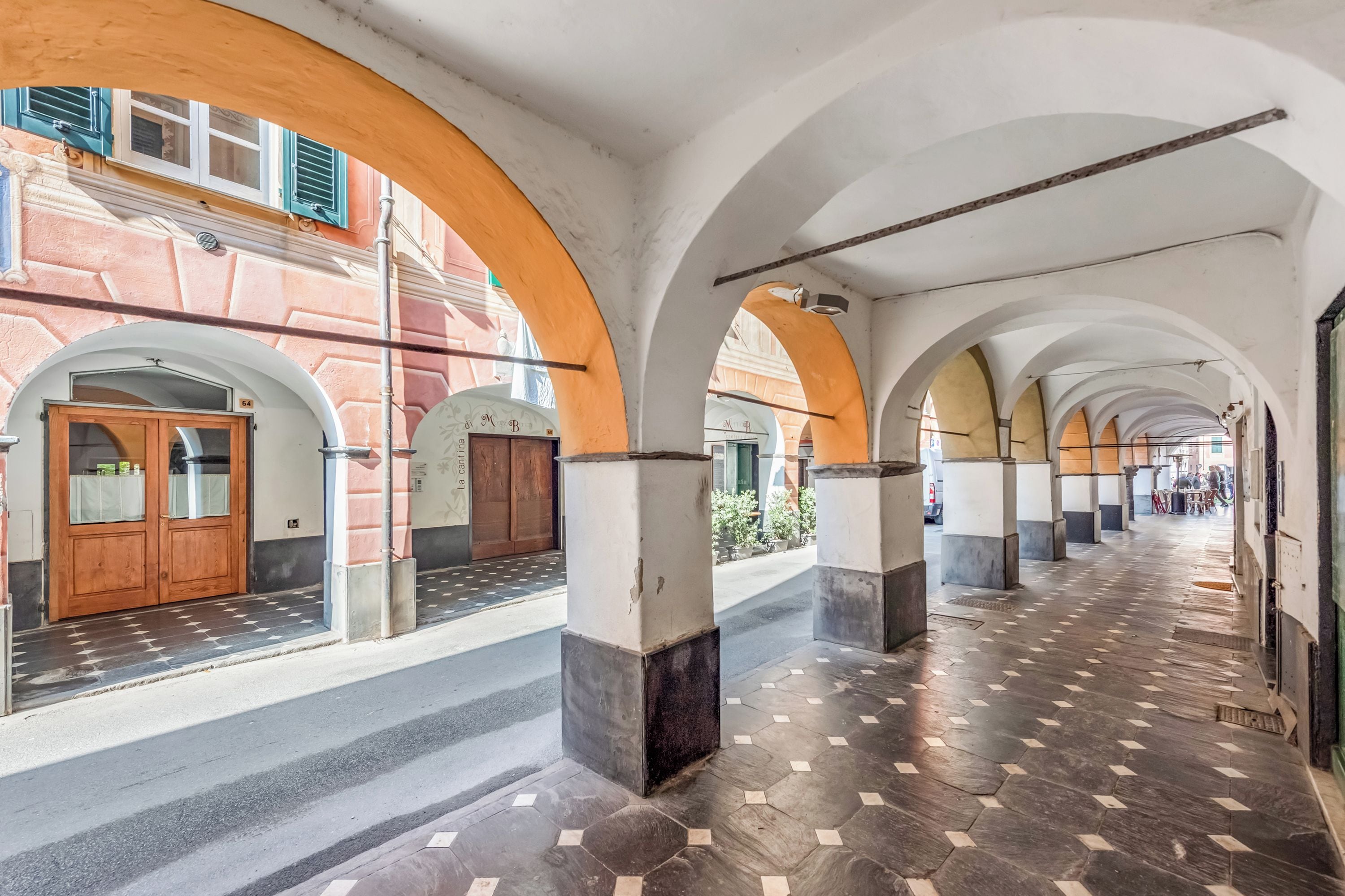 A corridor with arches, tiled flooring, and a building facade with a door and windows.