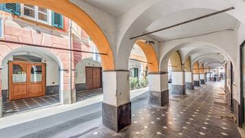 Un corridoio con archi, pavimento piastrellato e facciata di un edificio con una porta e finestre.