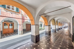 A corridor with arches, tiled flooring, and a building facade with a door and windows.