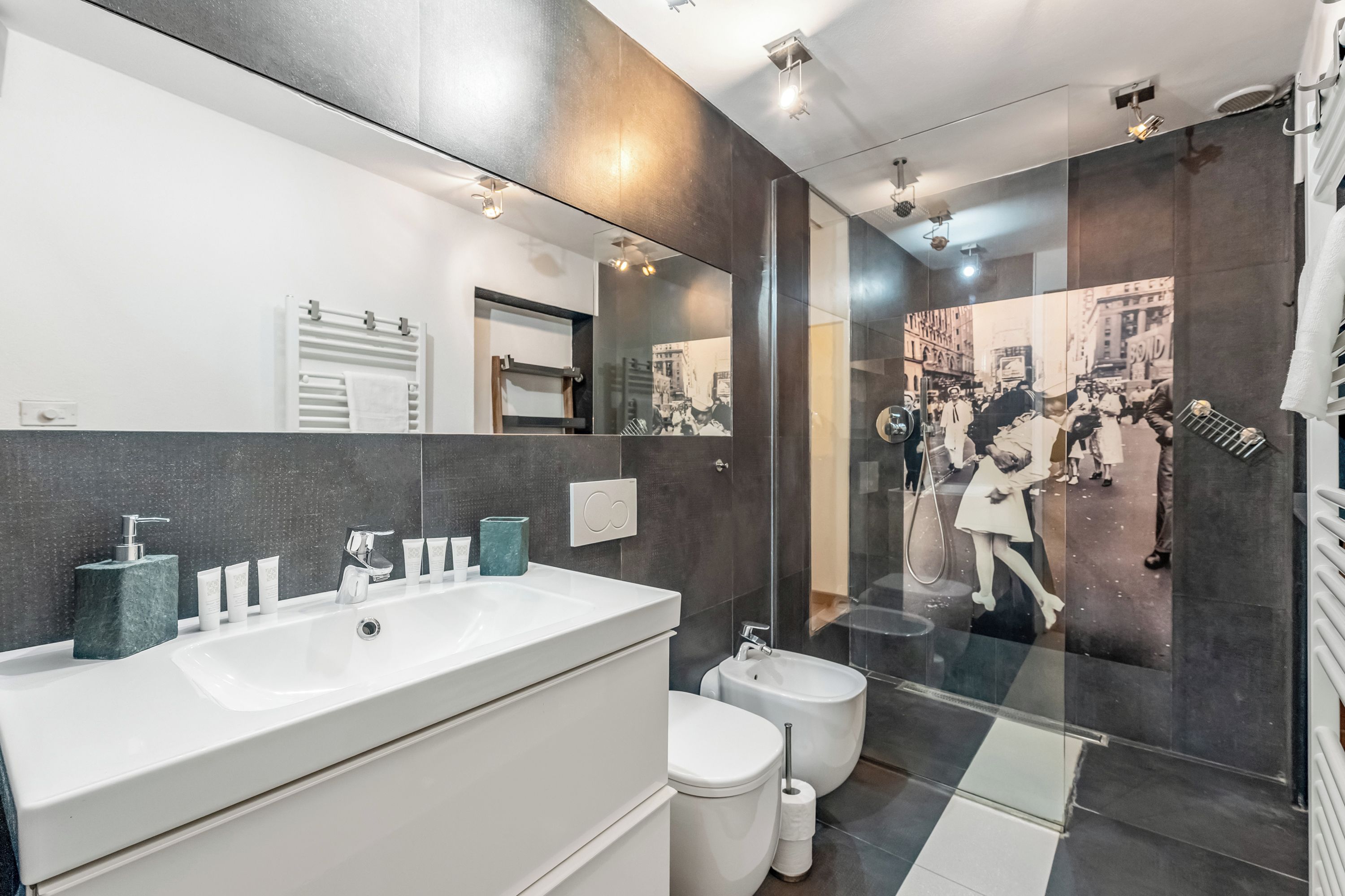 A modern bathroom with a large mirror, dual sinks, a bidet, and a glass shower enclosure.