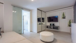 A modern living room with a sliding glass door, a flat-screen TV, a white ottoman, and a minimalist design. - Modern studio apartment with pool and terrace in Crikvenica near sandy beach (Crikvenica)