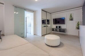 Ein modernes Wohnzimmer mit einer Schiebeglastür, einem Flachbildfernseher, einem weißen Hocker und einem minimalistischen Design.