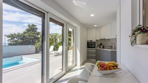 A modern kitchen with white cabinets, a dining area with a fruit bowl, and a poolside view. - Modern studio apartment with pool and terrace in Crikvenica near sandy beach (Crikvenica)