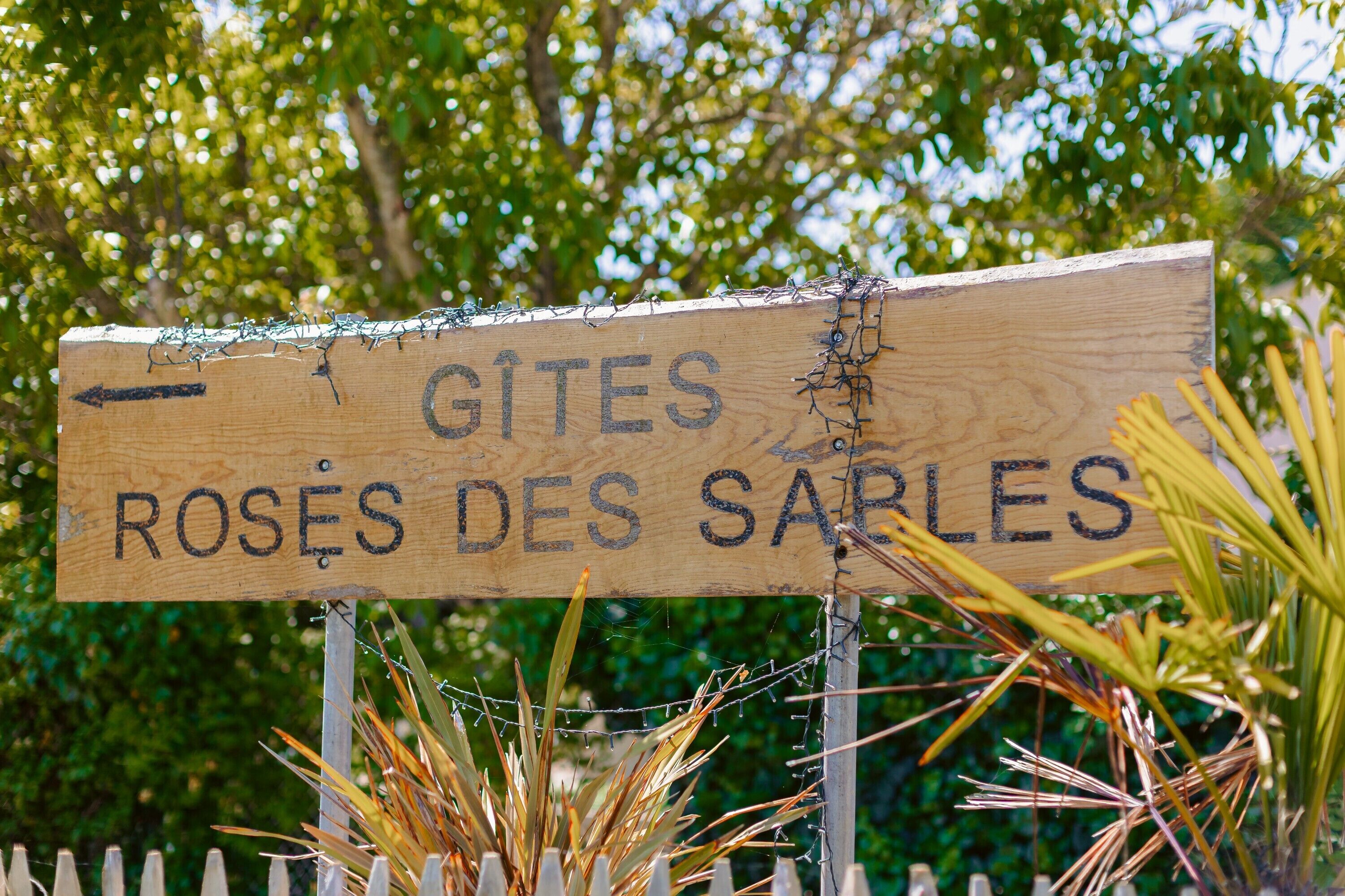 Ein hölzernes Schild mit dem Text 'GITES ROSES DES SARLES' und einem nach links zeigenden Pfeil.