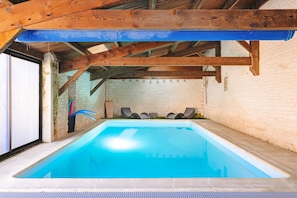 En indendørs swimmingpool med træloft og murstensvægge.