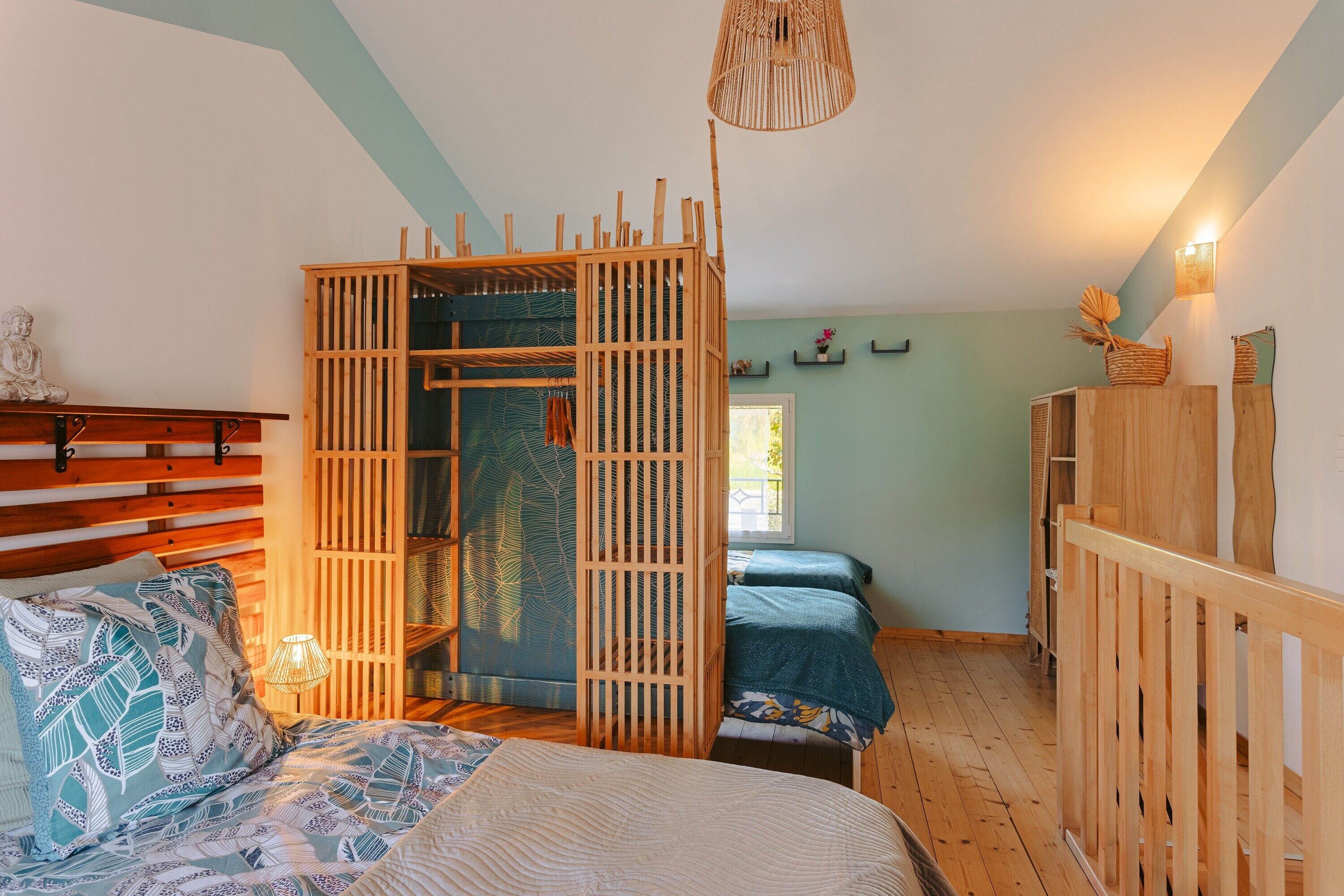 Una habitación con cama, un separador de madera, una silla colgante y una mesita de noche con lámpara.