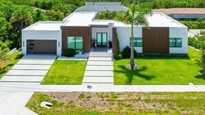 A modern two-story house with a garage, a covered patio, and a view of a body of water. - 4BR Marco Island home with heated pool, WiFi, and full kitchen. (Marco Island)