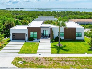 A modern two-story house with a garage, a covered patio, and a view of a body of water. - 4BR Marco Island home with heated pool, WiFi, and full kitchen. (Marco Island)