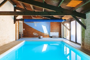 Une piscine intérieure avec des poutres en bois, un mur blanc et une grande fenêtre.
