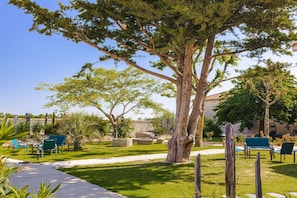 Un jardin avec un grand arbre, des sièges extérieurs et un mur en pierre.