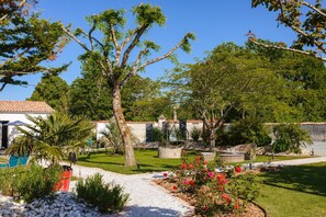 Un jardin avec un chemin, une piscine et un bâtiment doté d’un toit en tuiles.