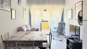 Zona pranzo con tavolo, sedie, televisore e finestra con tende.