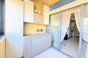 Una cucina con armadi, un piano di lavoro e una porta scorrevole in vetro che dà su un balcone.