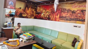 A room with a green sofa, a desk with a calculator and papers, and a wall with a mural. - The Kashi Iconic Guest House (Varanasi)