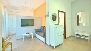Ein modernes Wohnzimmer mit Flachbildfernseher, einer Couch, einem kleinen Tisch und einem weißen Schrank.