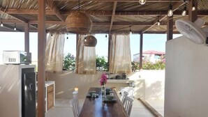 A covered outdoor dining area with a table set for two, a fan, and a refrigerator in the background. - Loft Boutique *Starlink | Private Pool * La Punta (La Barra de Colotepec)