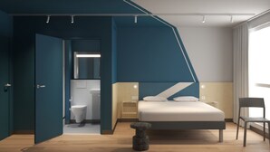 A modern bedroom with a bed, a chair, a small stool, and a bathroom visible through an open door. - ibis budget Guingamp - Coeur de Bretagne (October 2026) (Ploumagoar)