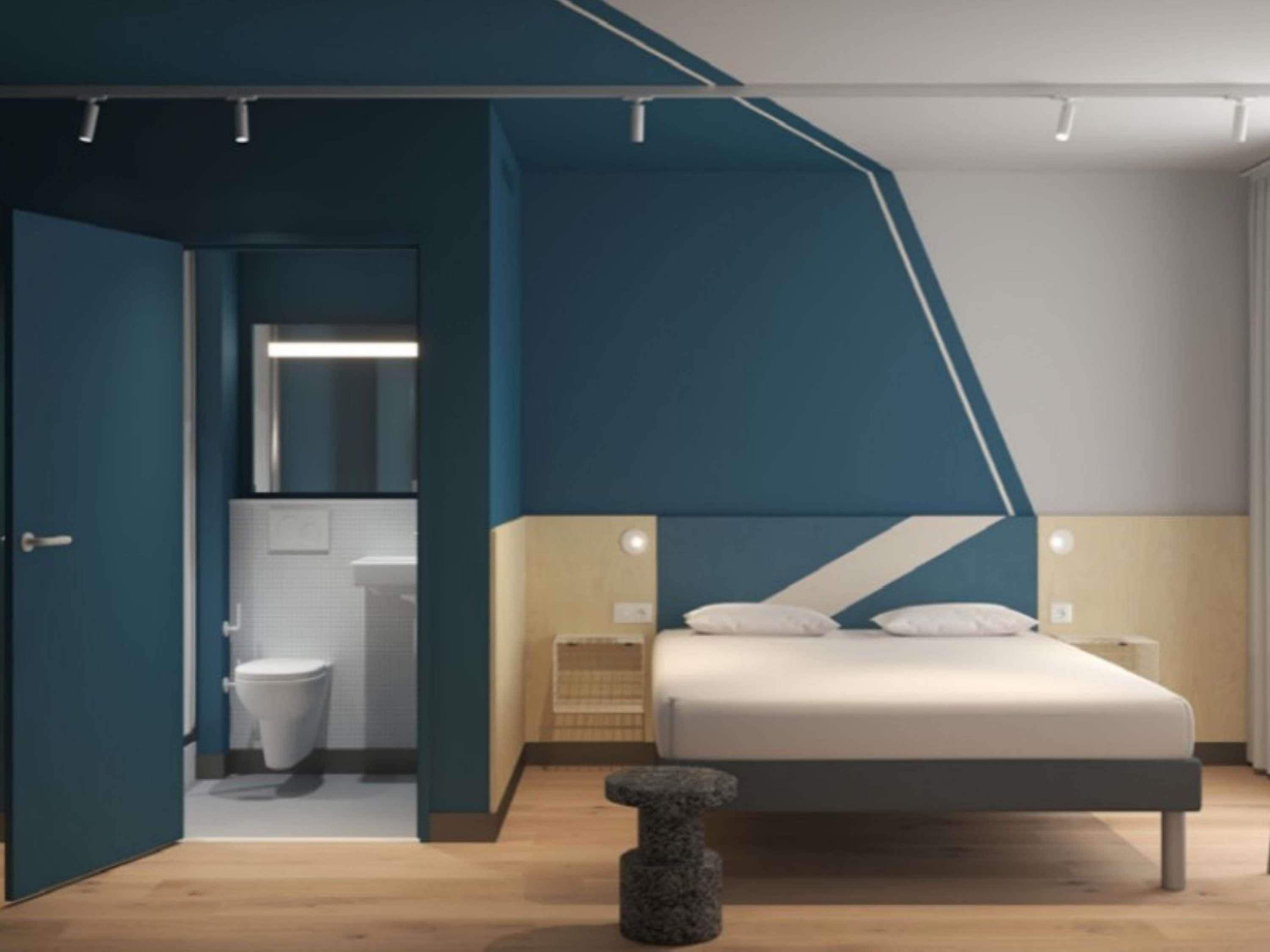 A modern bedroom with a bed, bedside tables, and a bathroom visible through an open door.