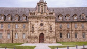 Um edifício histórico com fachada simétrica, janelas em arco e entrada central com um relógio.