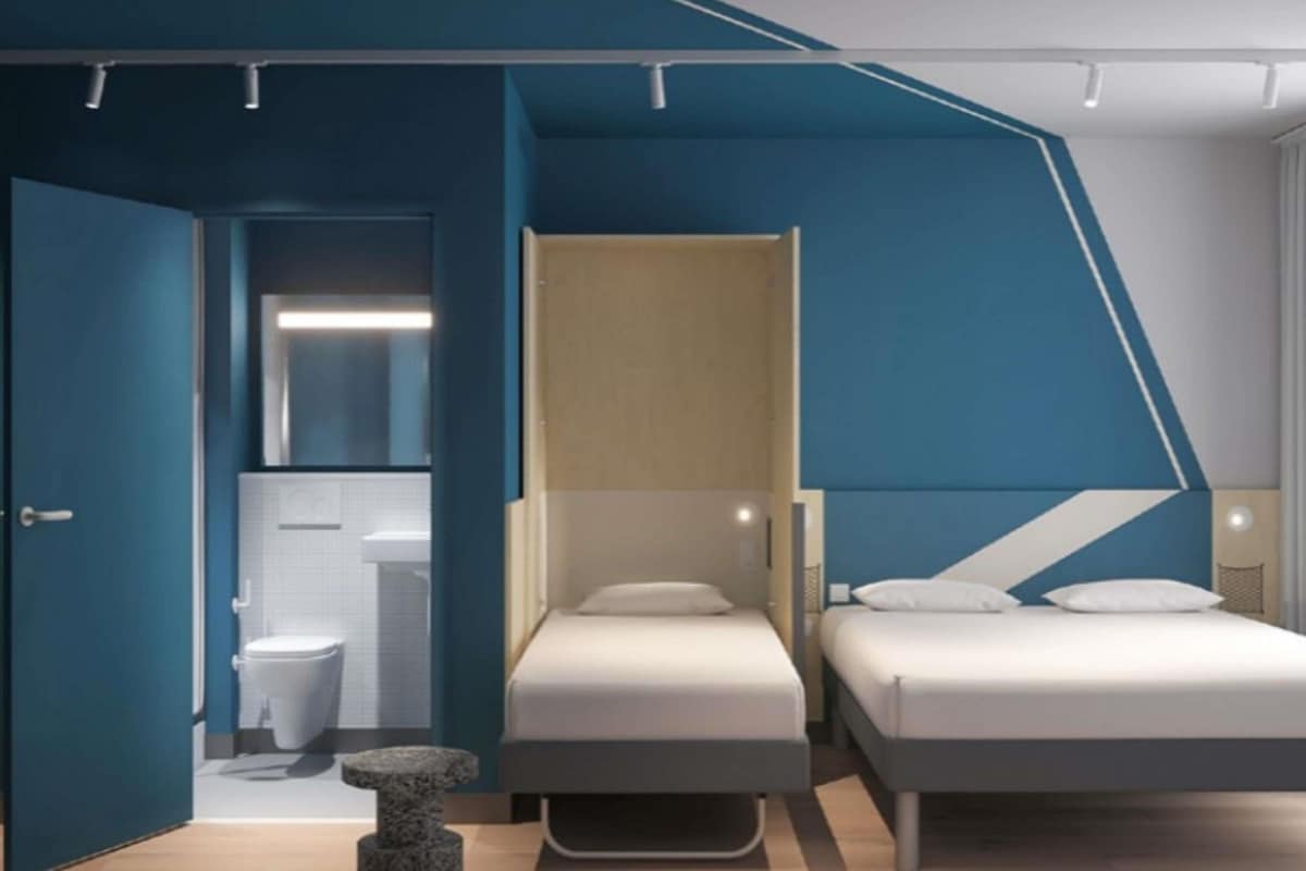 A modern bedroom with a sloped ceiling, a bed, a small table, and a bathroom visible through an open door.