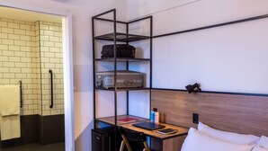 Habitación de hotel con una cama, un escritorio con silla, una pequeña cocina americana, un baño con toallero y un estante con equipaje.