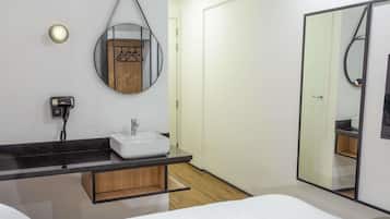 Ein modernes Hotelzimmer mit einem großen Bett, einem Nachttisch, einem Badezimmer mit Waschbecken und Spiegel sowie einem Kleiderschrank.