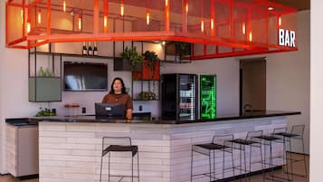 Uma área de bar com teto em tela vermelha, um bartender no balcão e um letreiro de neon verde.