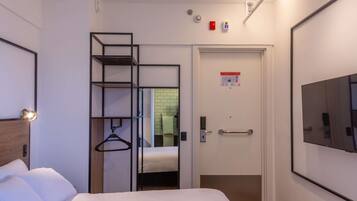 Quarto de hotel com cama, guarda-roupa com espelho, porta com puxador e televisão presa à parede.