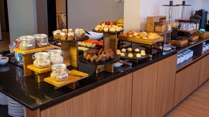 Un bufé con diferentes opciones de comida, incluyendo recipientes con cereales, pasteles y frutas.