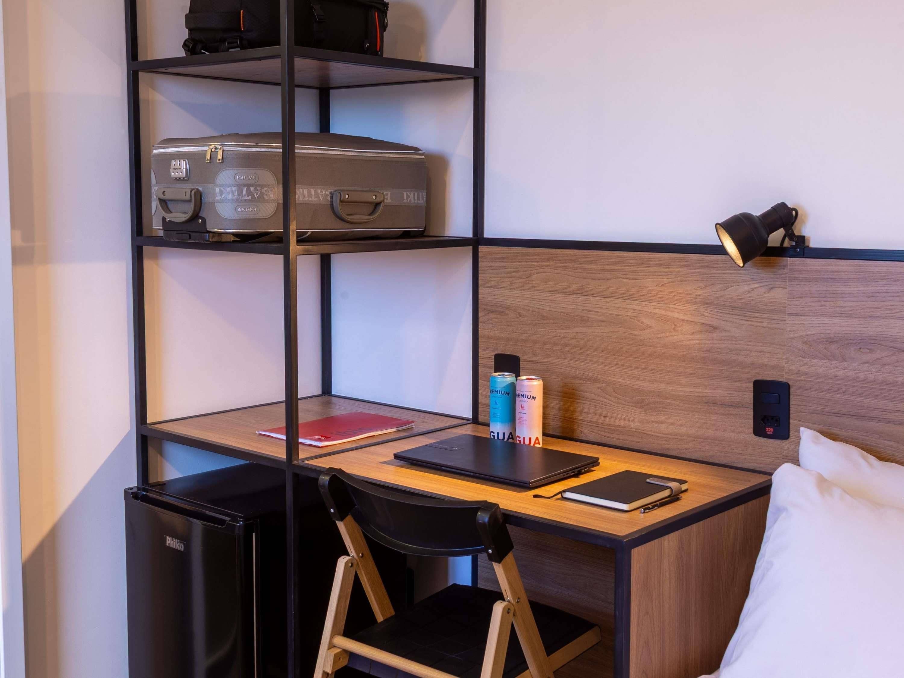 Ein kleines Hotelzimmer mit Schreibtisch, Stuhl und einer kompakten Küchenzeile.