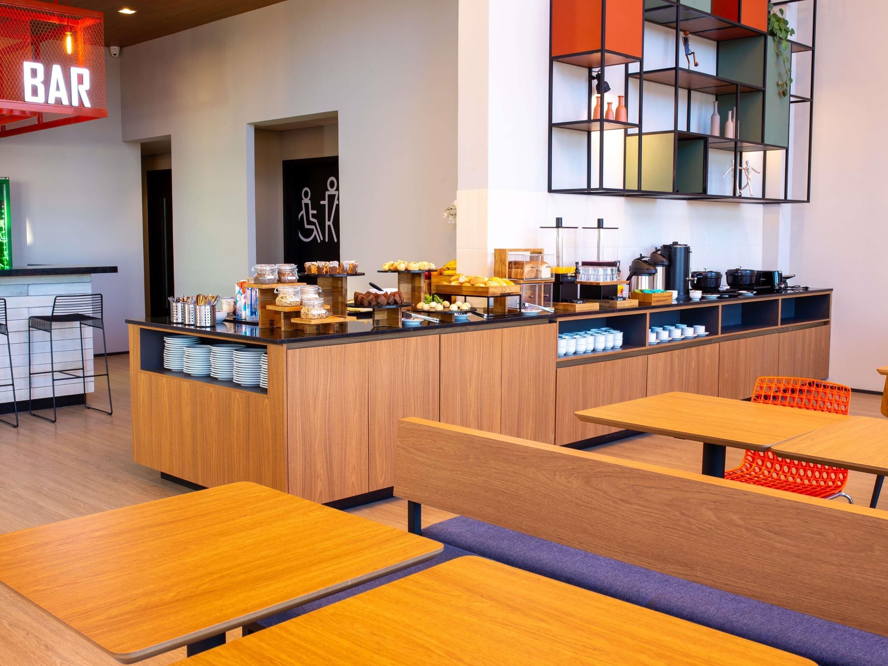 Um café moderno com área de bar, um balcão de buffet com diversos alimentos e diferentes opções de assentos.