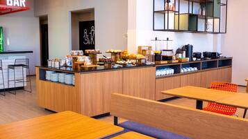 Um café moderno com área de bar, um balcão de buffet com diversos alimentos e diferentes opções de assentos.